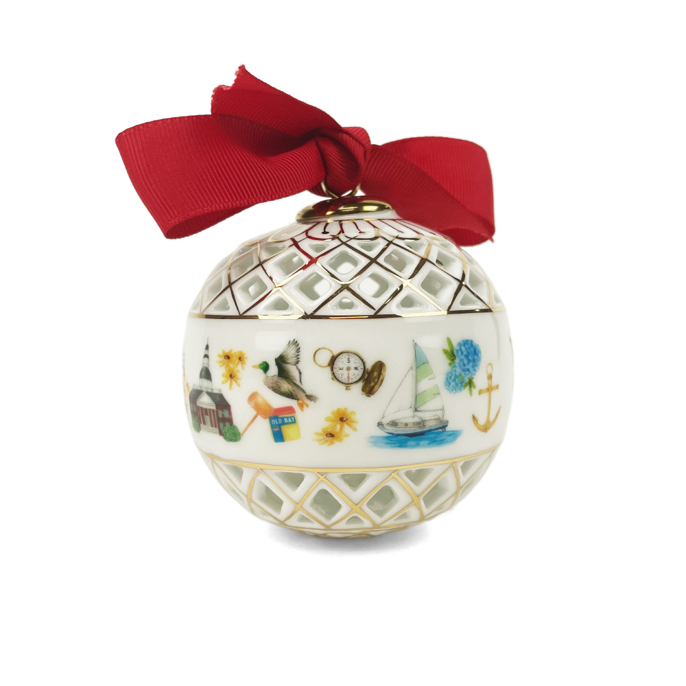 A white ceramic Christmas ornament decorated with gold lattice patterns, colorful nautical and holiday illustrations, and a red satin bow at the top, shown on a white background.