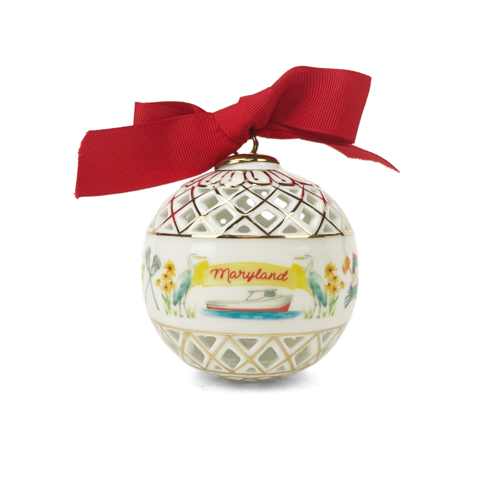A decorative Christmas ornament shaped like a white glass bauble with a red ribbon bow. The ornament features a gold lattice pattern on the top and bottom, a yellow banner reading 'Maryland' with a small boat, and painted flowers and birds.