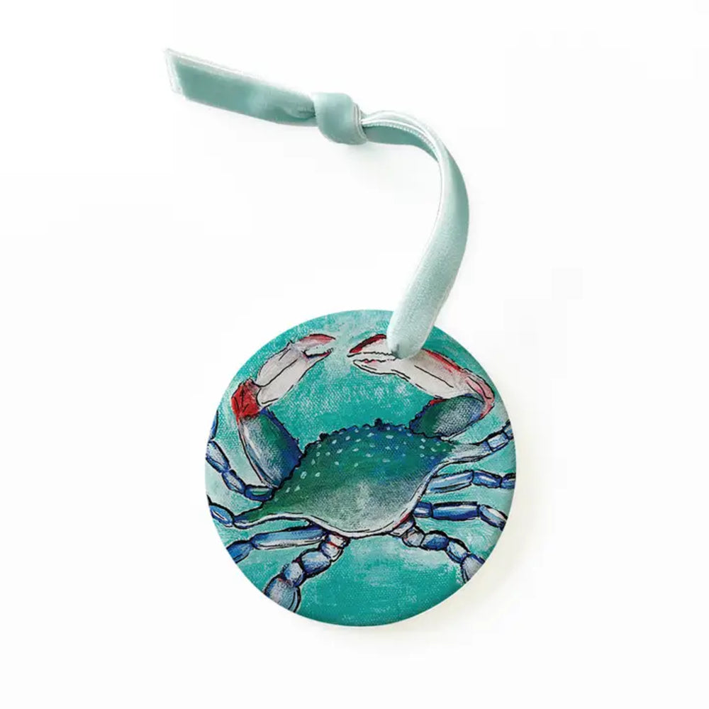 A round decorative tag featuring a painted blue crab on a turquoise background, with a light blue ribbon loop at the top, shown on a plain white background.
