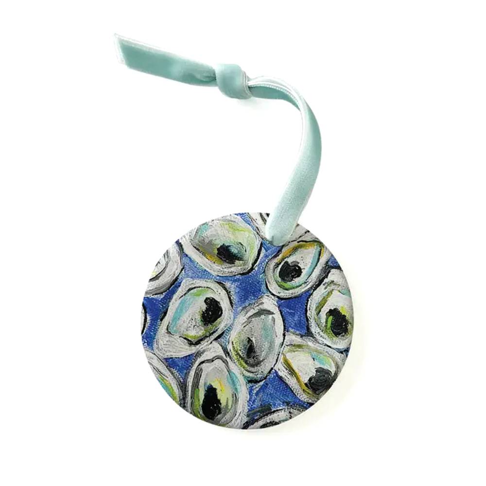 A round printed ornament featuring a blue and white oyster shell pattern, suspended by a mint green ribbon on a white background.