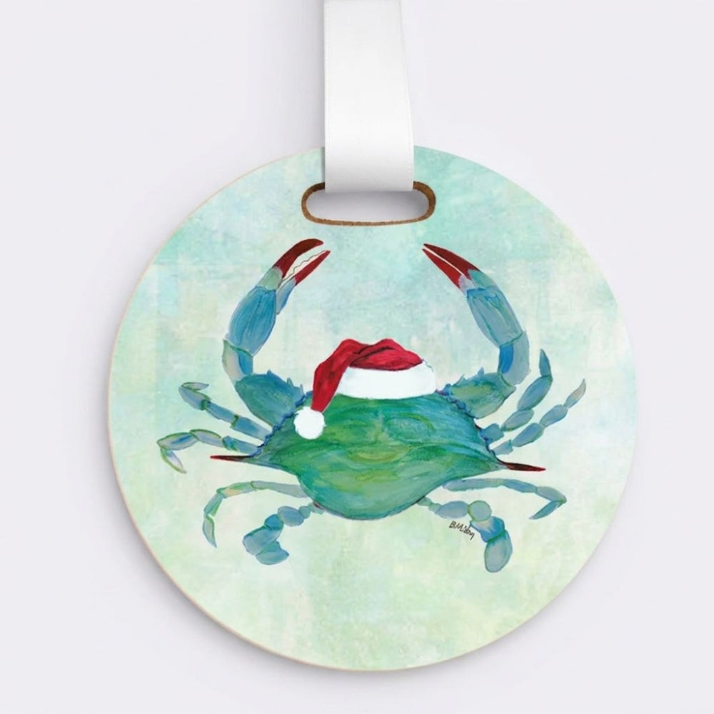 Round wooden Christmas ornament featuring a painted blue crab with a red Santa hat, hanging from a white ribbon on a light gray background.