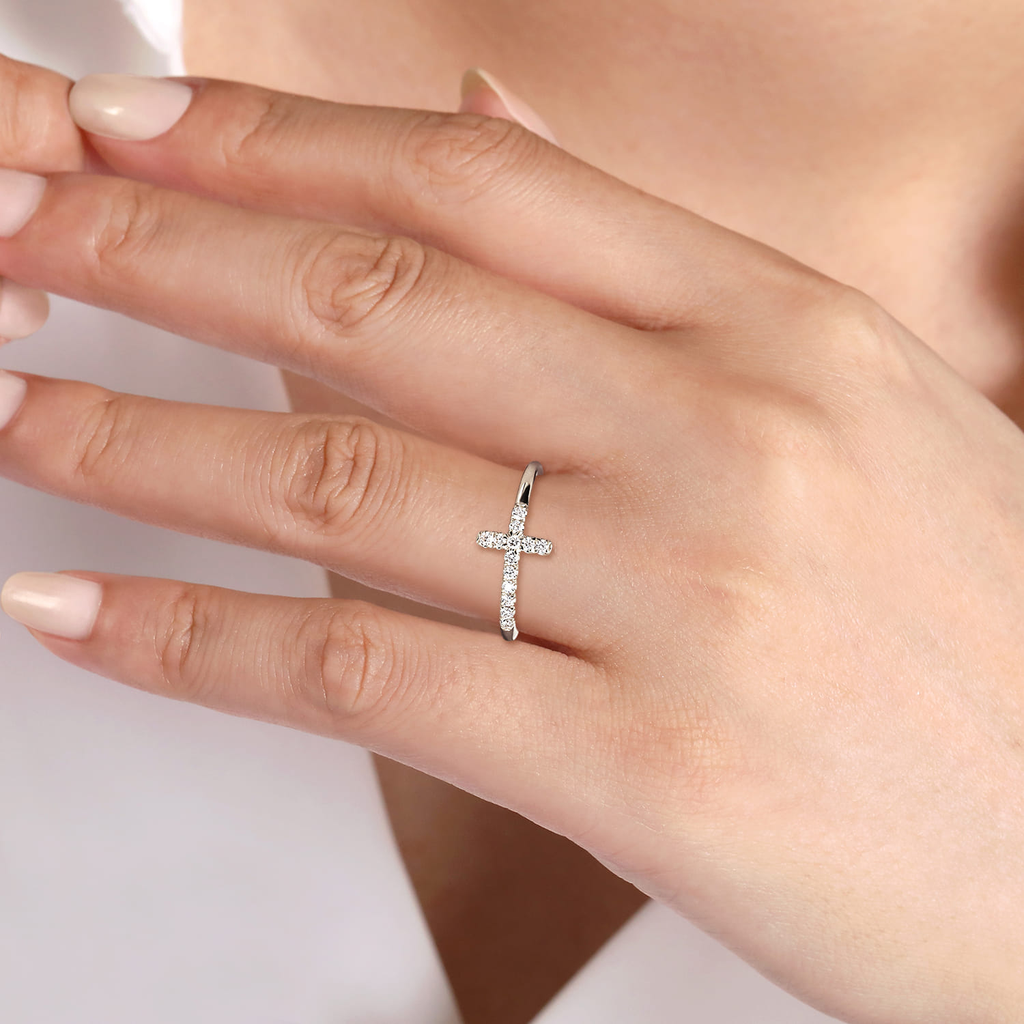 Silver cross-shaped ring on a person's finger with a soft background