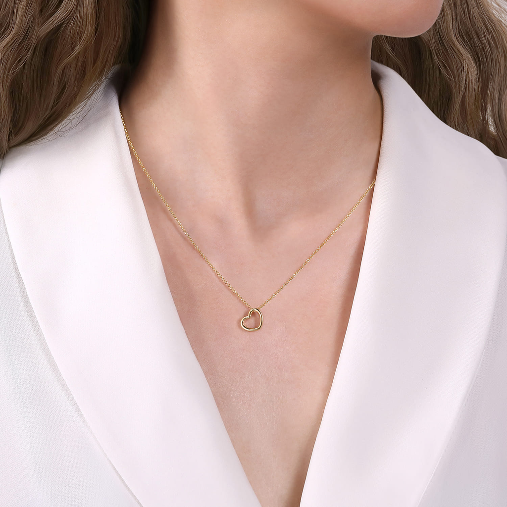 Gold necklace with a heart pendant worn by a person in a white blazer.