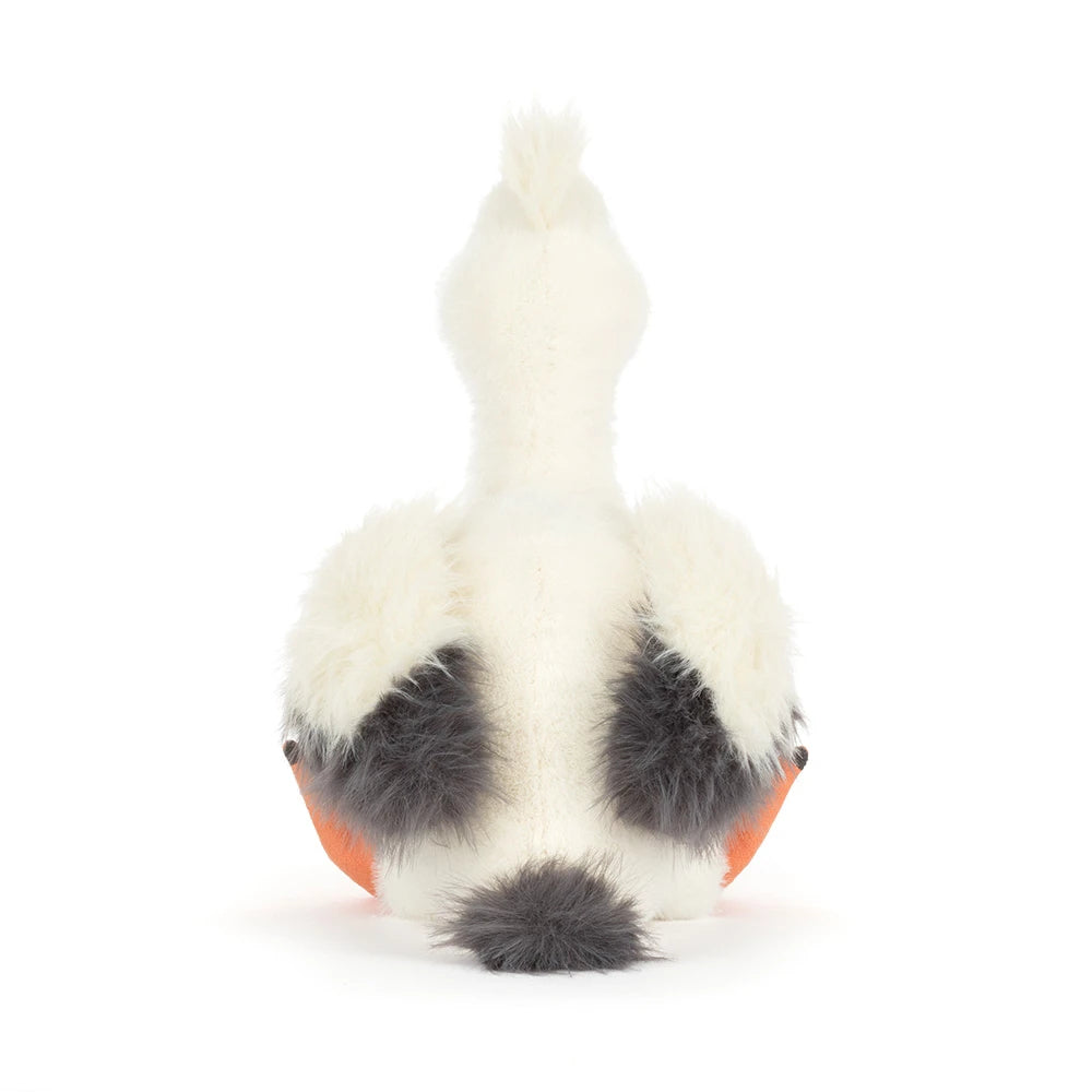 A photo of the back of an Keli Pelican stuffed animal with a white and grey body and orange beek and legs on a white backround.