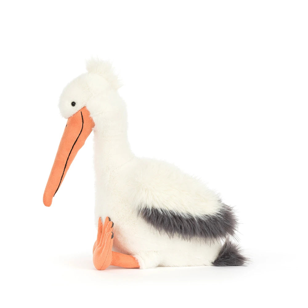 A side photo of an Keli Pelican stuffed animal with a white and grey body and orange beek and legs on a white backround.