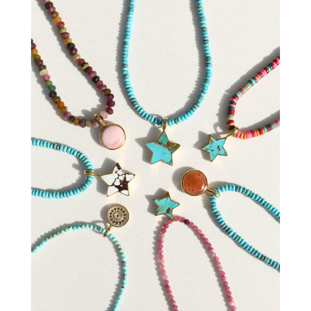 Six colorful beaded necklaces and bracelets arranged on a light beige background, featuring turquoise, pink, orange, and brown beads with star and oval charms.