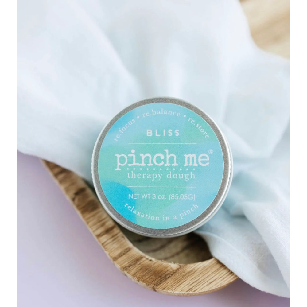 A tin lid of Bliss pinch me therapy dough on a white cloth background.
