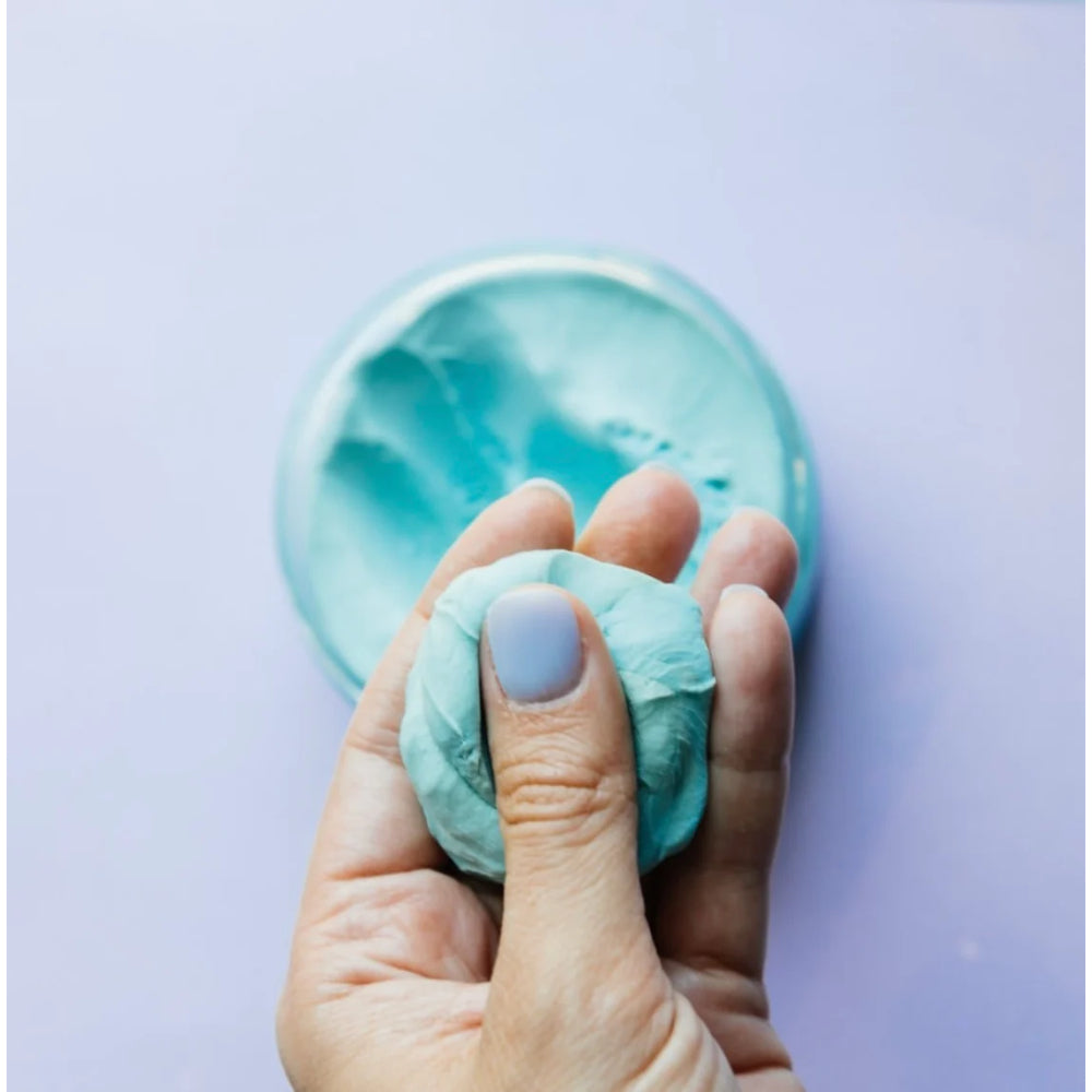 Hand holding a small ball of blue therapy dough with a purple background.