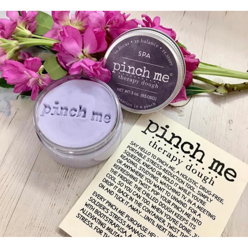 Two containers of 'pinch me' therapy dough with a bouquet of pink flowers on a wooden surface.