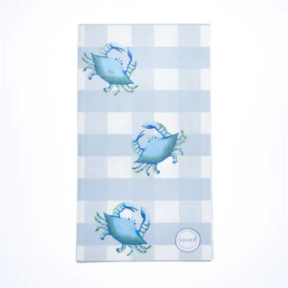 A rectangular kitchen napkin with a light blue and white gingham check pattern, decorated with three blue crabs and a small circular 'shard' brand logo in the bottom right corner.