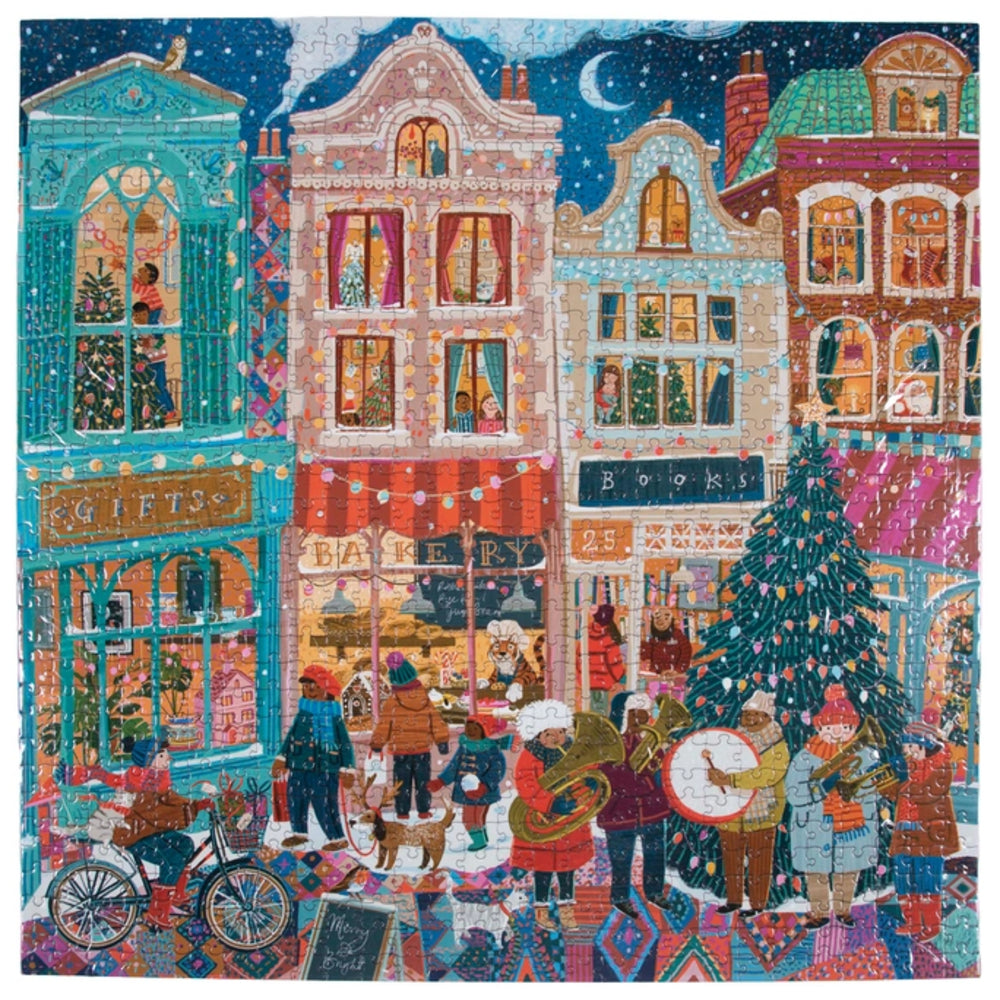 A colorful square art print depicting a whimsical Christmas village street scene with multi-story buildings, storefronts, people gathered around a decorated Christmas tree, and a night sky with a crescent moon.