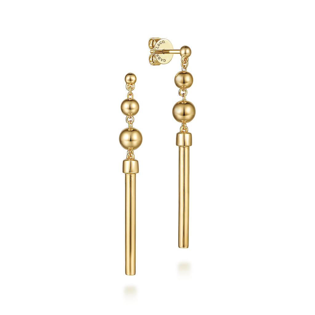 Gold earrings with spherical beads and a long cylindrical drop on a white background