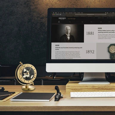 Computer monitor displaying a Seiko website on a desk with a world globe and office supplies.