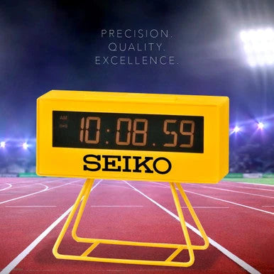 Yellow Seiko digital clock on a track with 'PRECISION. QUALITY. EXCELLENCE.' text above
