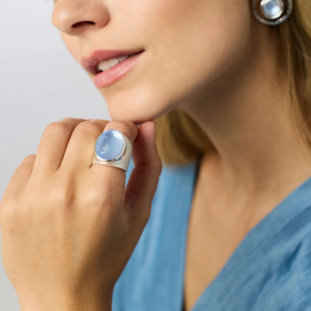 Woman wearing a ring with a blue gemstone and matching earring on a neutral background