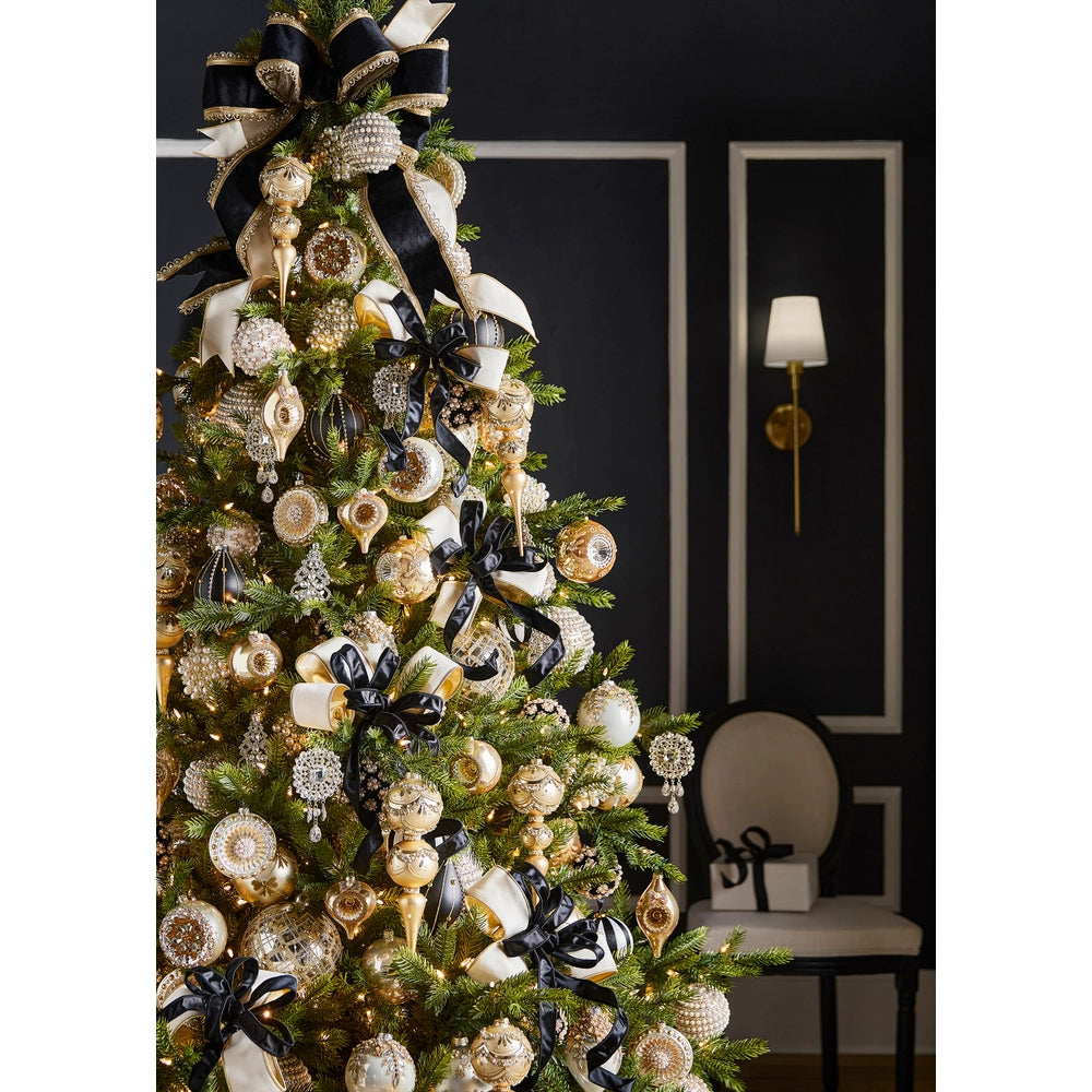 Decorated Christmas tree with gold, black, and white ornaments against a dark wall.