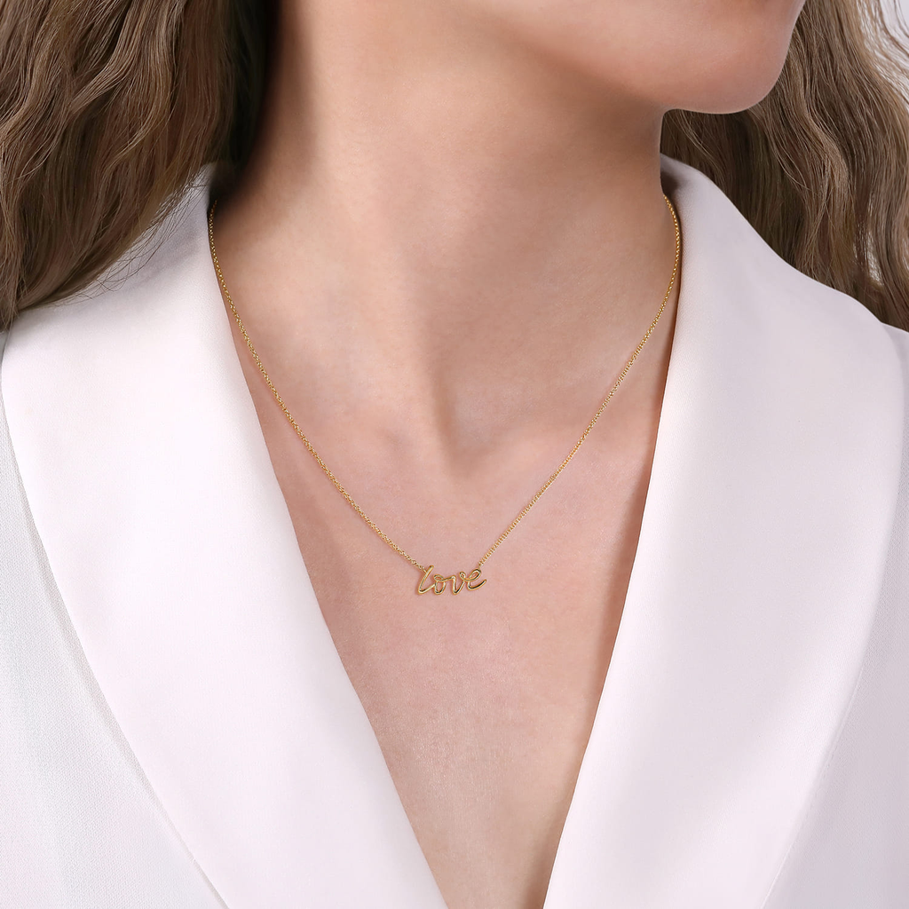 Gold necklace with 'love' pendant worn by a person in a white outfit