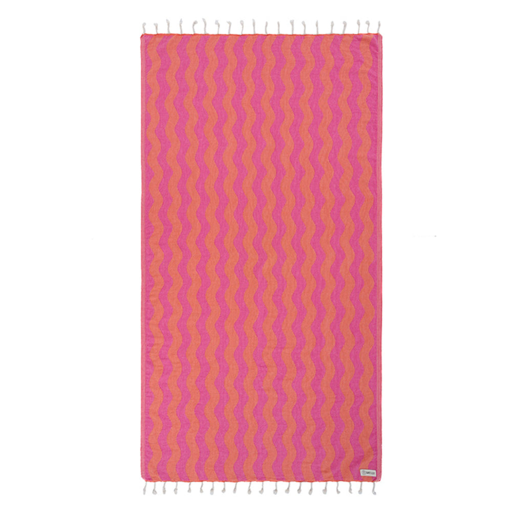 Coral pink and orange wavy patterned beach towel with white fringe edge on a white background. 