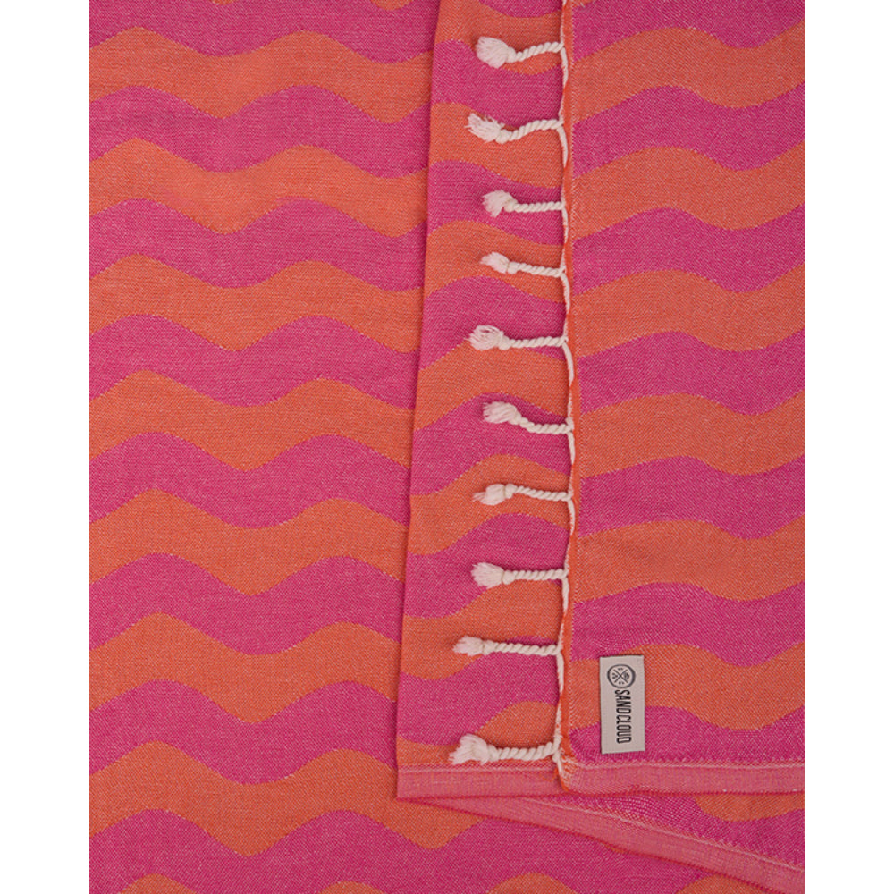 close up of the coral pink and orange wavy patterned beach towel with white fringe edge on a white background. 