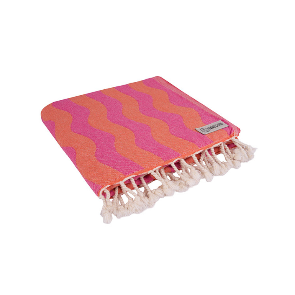 Folded coral pink and orange wavy patterned beach towel with white fringe edge on a white background. 