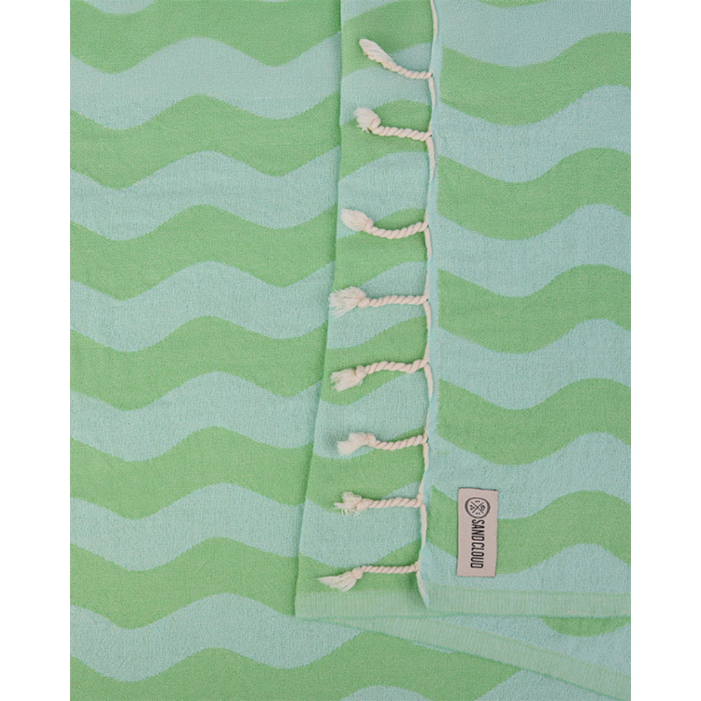 Close up of a lime green and blue wavy striped beach towel with white tassel edge and a brand logo on a white background