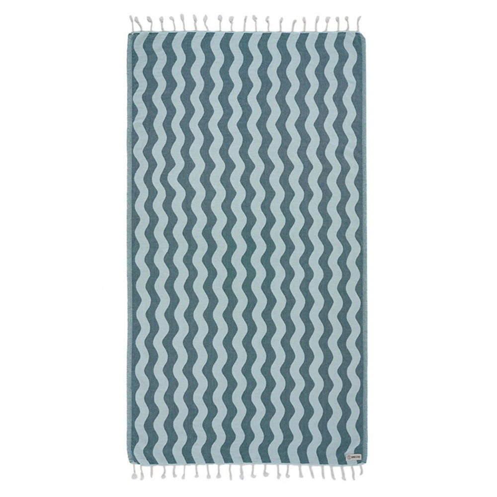 Teal blue beach towel with blue wavy stripes and  white tassel edge on a white background.