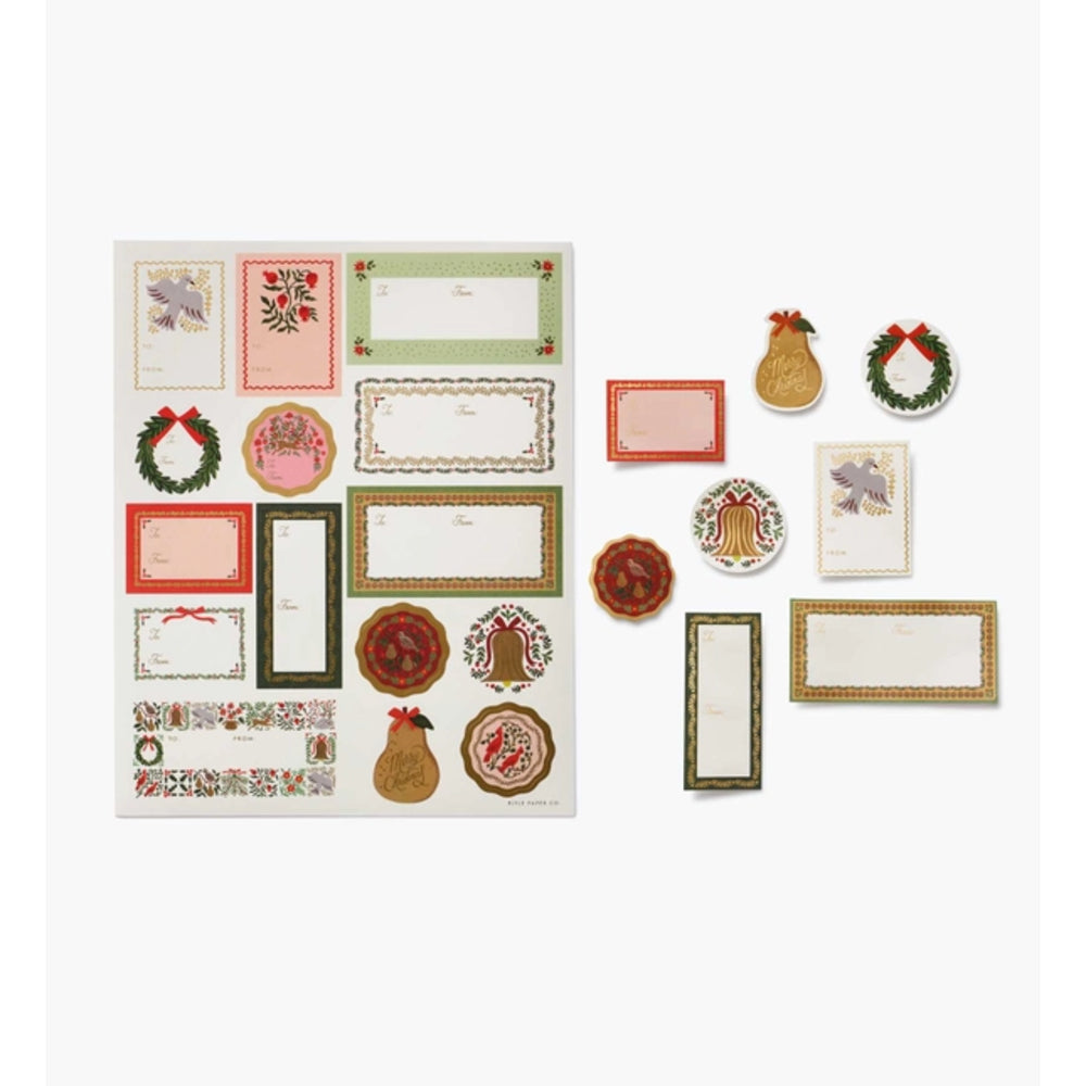 A set of Christmas-themed paper cutouts and decorative labels arranged on a white background, including wreaths, pears, bells, floral frames, and blank name cards.