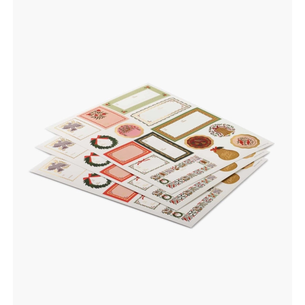 Four sheets of decorative Christmas-themed stickers fanned out on a light gray background. The stickers feature festive designs including wreaths, gift boxes, ornaments, and labels in red, green, gold, and beige tones.