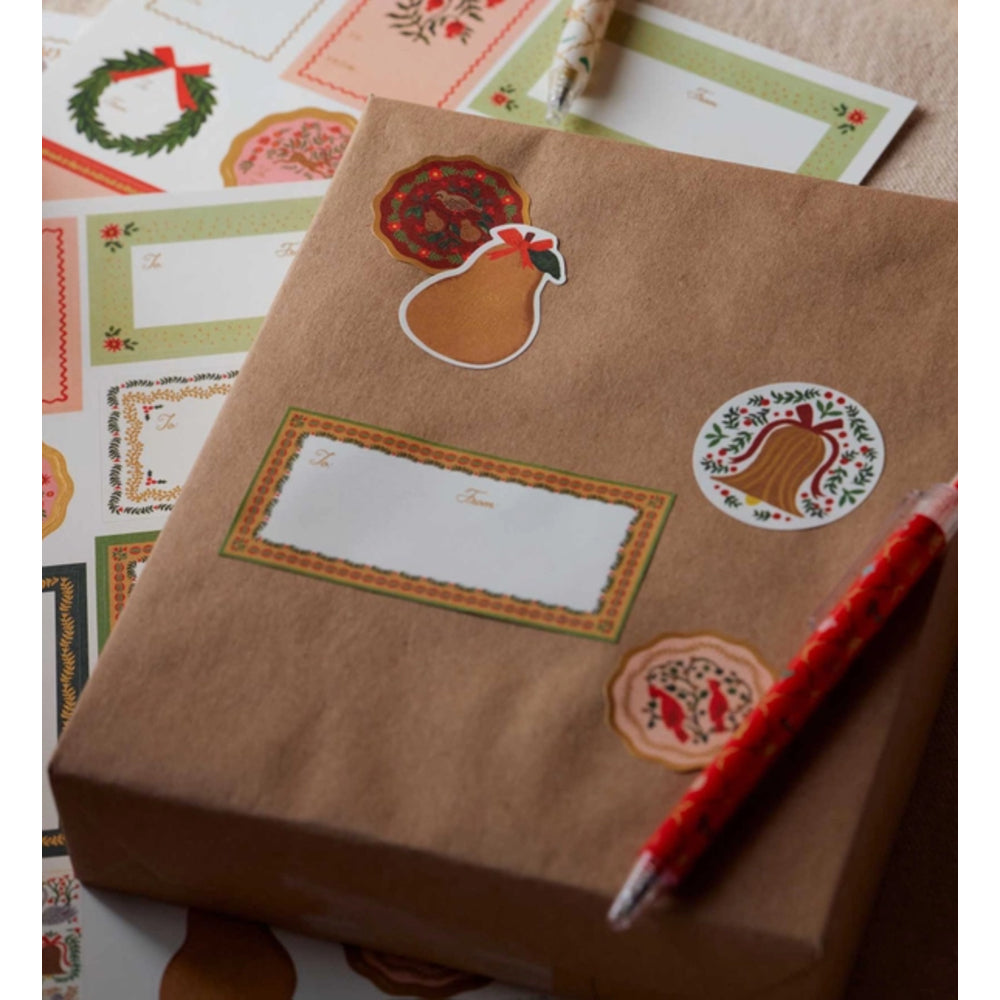 A brown kraft paper gift box decorated with autumn-themed stickers, including a turkey sticker, a pear-shaped ornament, and a rectangular label, with a red patterned pencil resting on top.