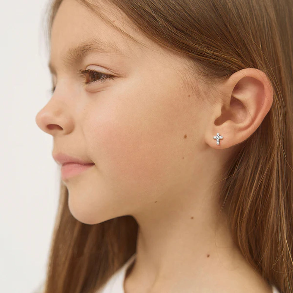 Close-up of a young girl wearing a small cross earring on a plain background