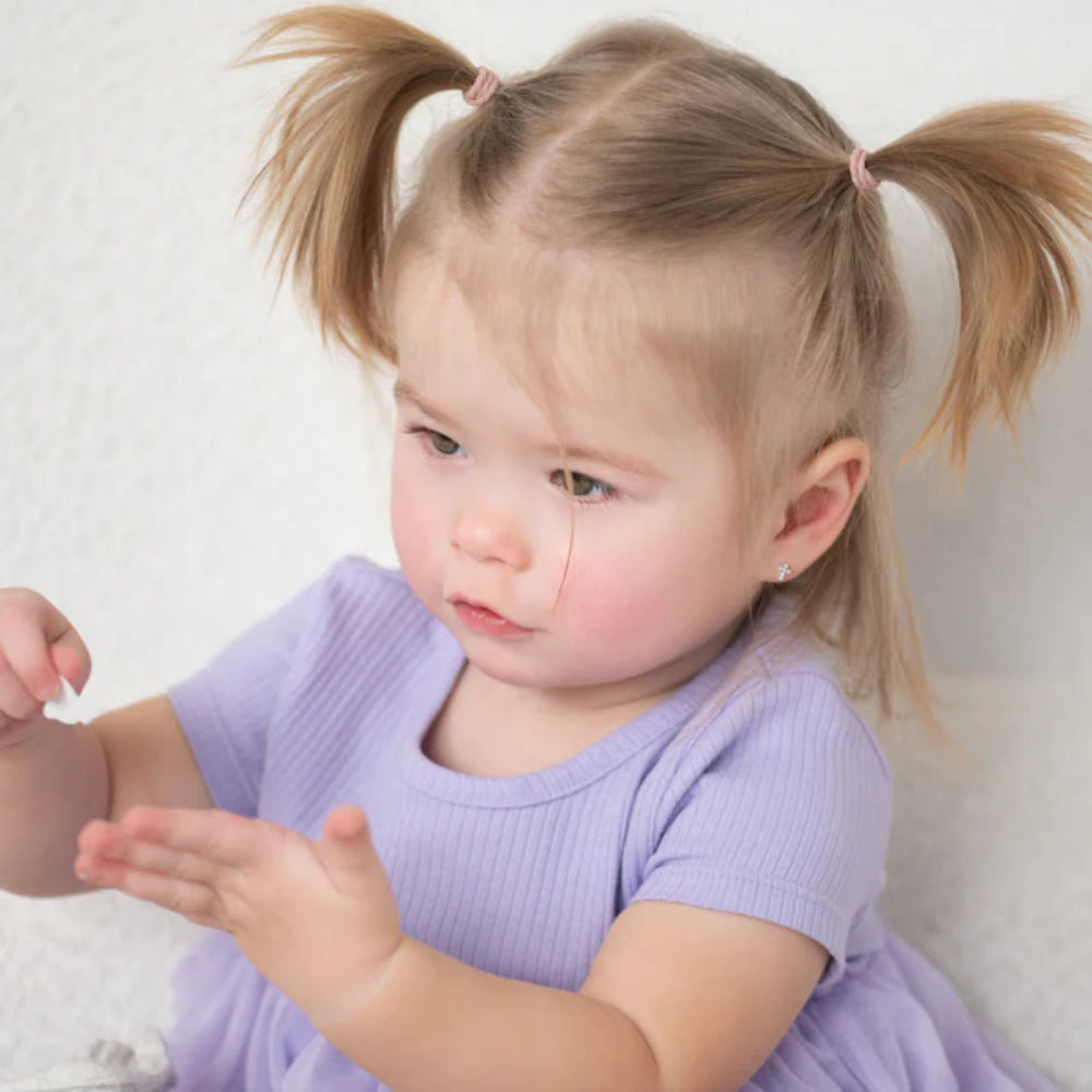 Child with pigtails wearing a purple shirt against a white background
