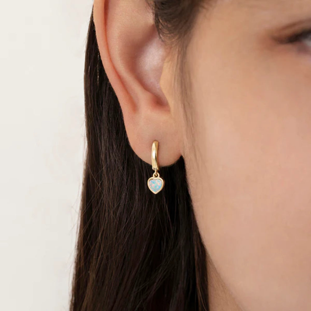 Gold heart-shaped earring worn by a person with a neutral background