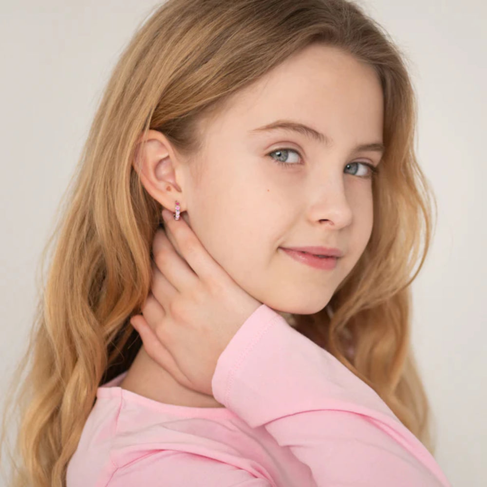 Young girl wearing pink earrings with a plain background