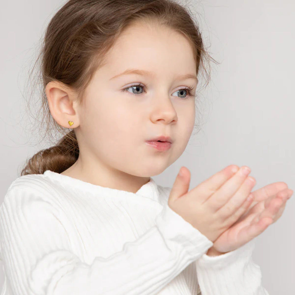 Young girl with a heart-shaped earring blowing bubbles against a light background