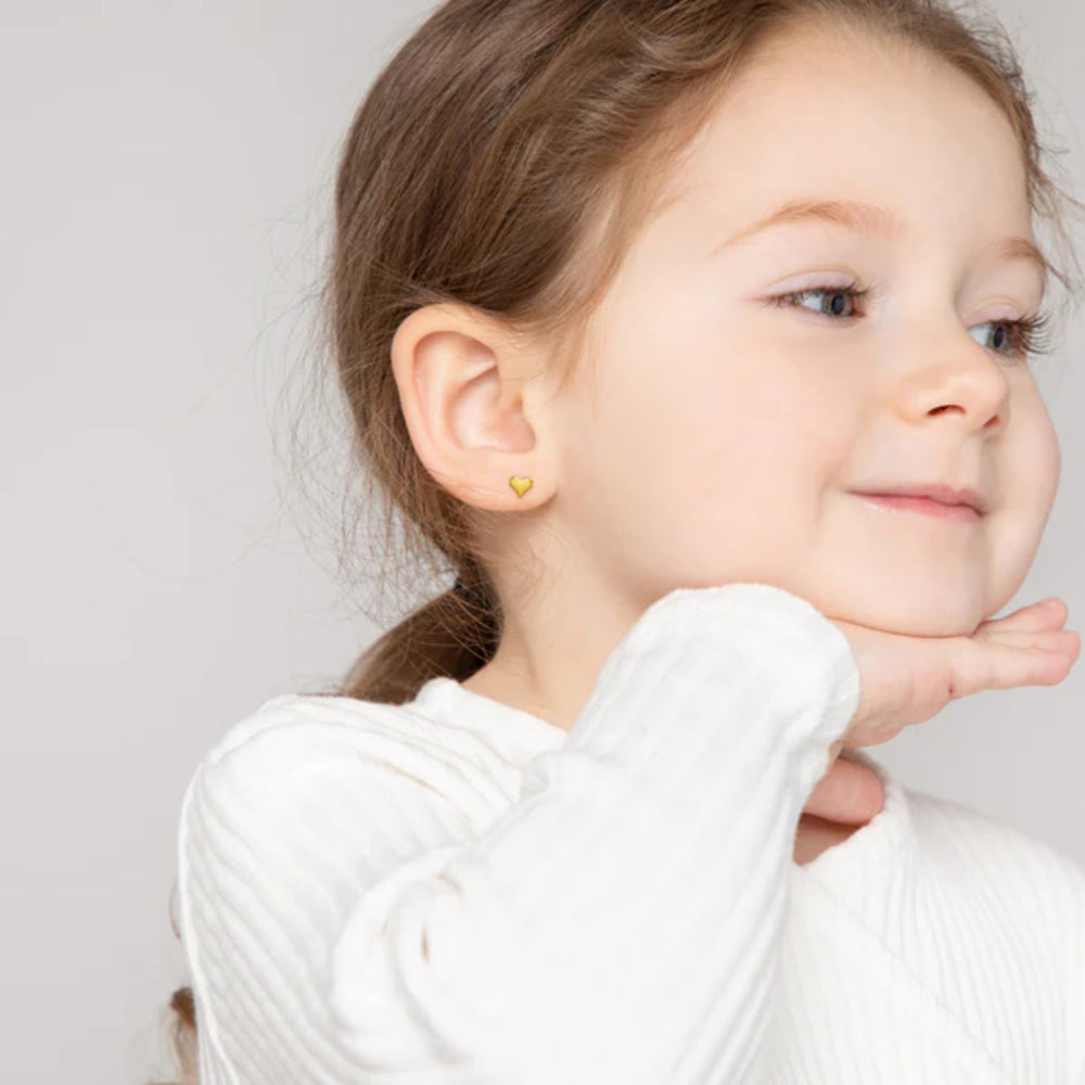 Young girl wearing gold heart-shaped earrings against a plain background