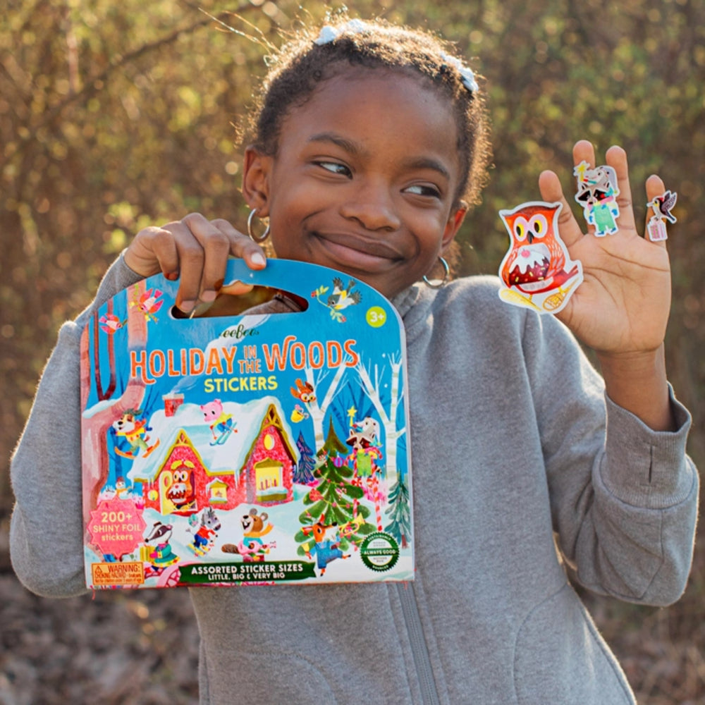 Child holding a 'Holiday in the Woods' stickers product with two stickers in front of a natural background.