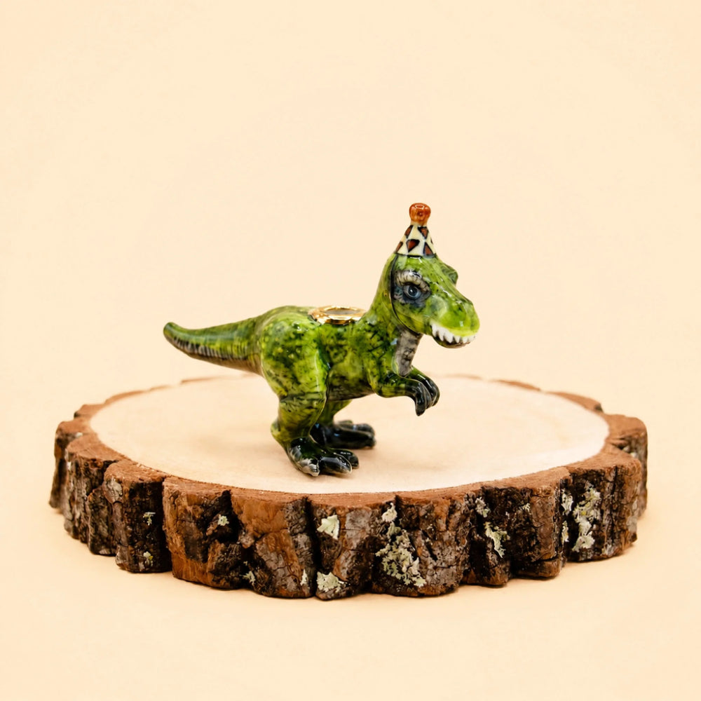 A green dinosaur figurine with a small pointed hat, displayed on a rustic wood slice coaster against a warm beige background.