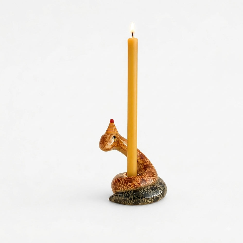 A coiled snake-shaped candle holder with a lit taper candle inserted into its head, set against a solid warm beige background.