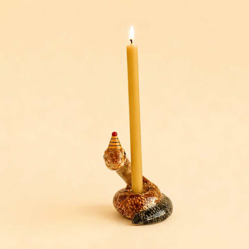 A snake-shaped candle holder with a lit taper candle, set against a solid warm beige background.