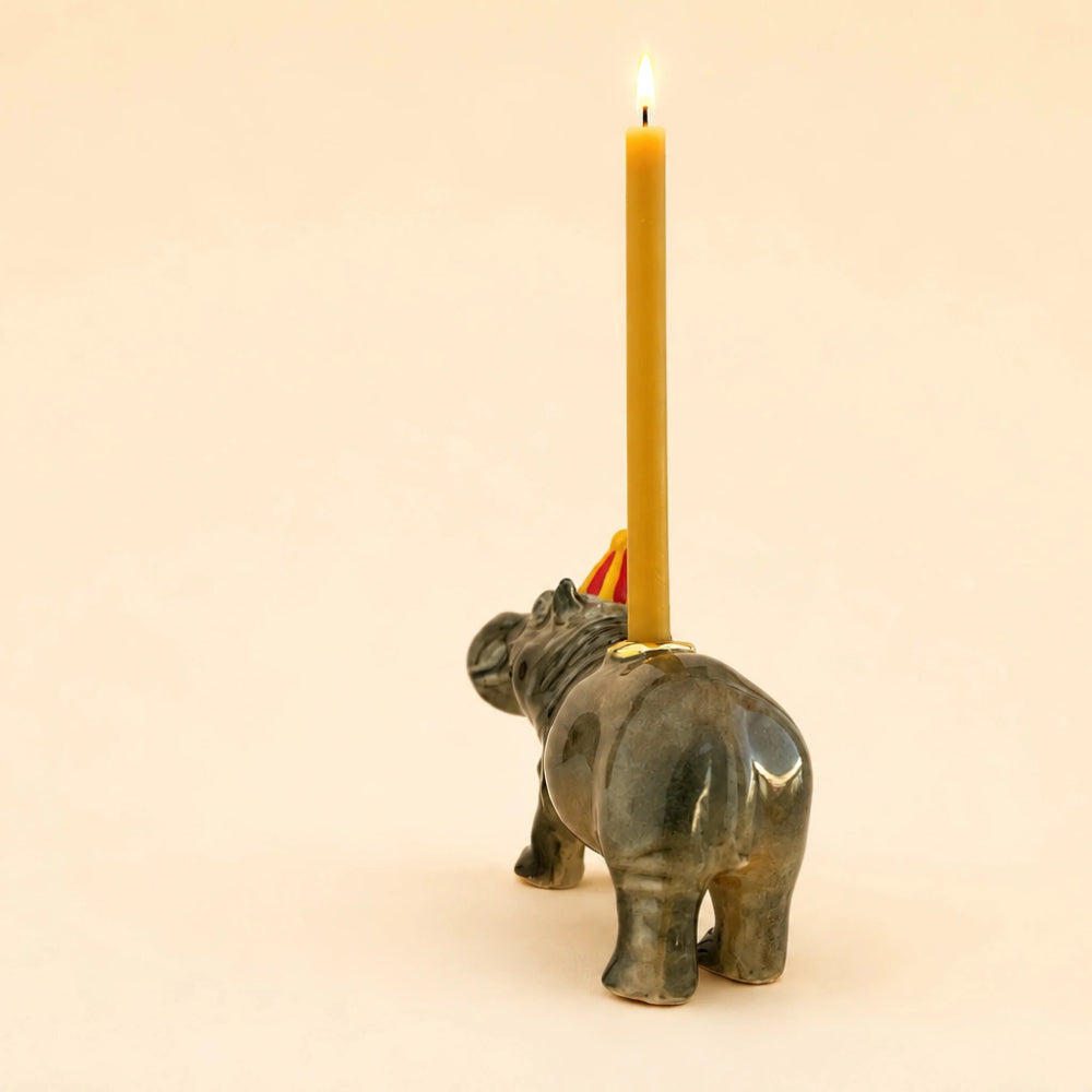 A small elephant-shaped holder in a dark metallic finish holding a lit yellow candle, photographed against a plain warm beige background.