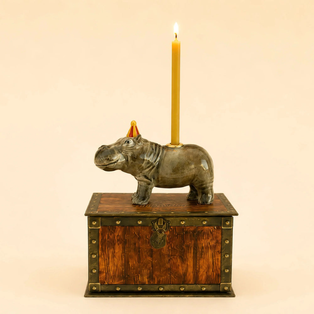 A rhinoceros-shaped candle holder made of dark metal, sitting on top of a small wooden chest with brass trim. A lit yellow candle is inserted into the back of the rhinoceros.