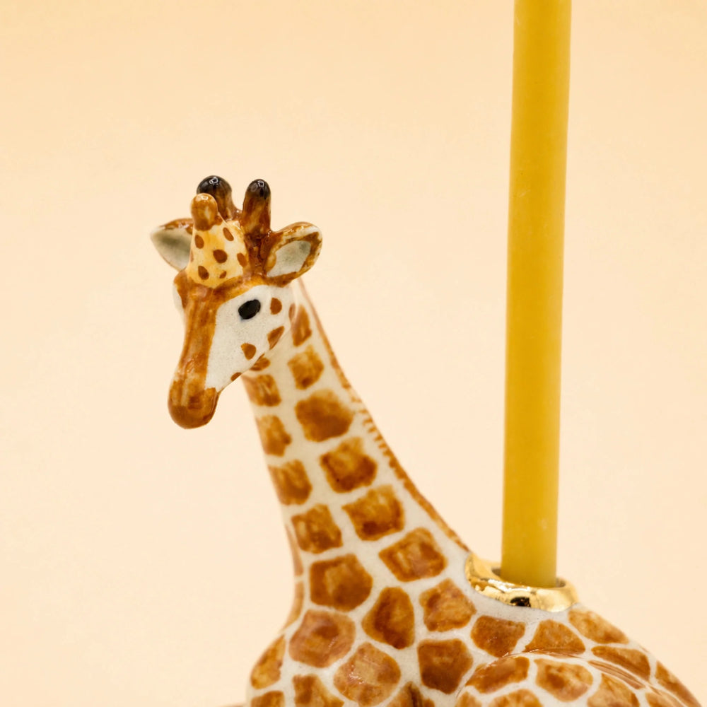 Close-up of a giraffe-shaped candle holder with a yellow candle inserted into the neck, set against a plain beige background.