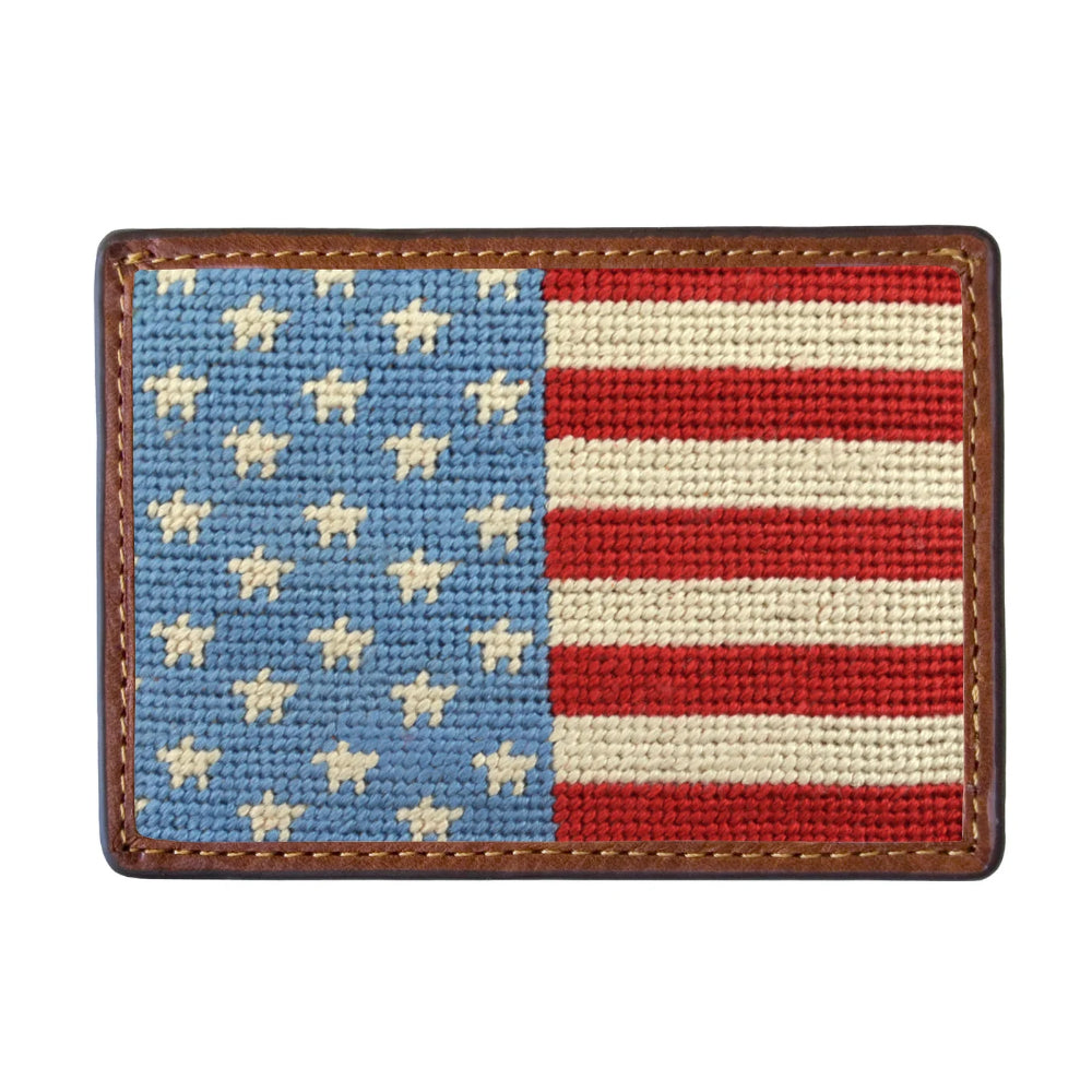 A rectangular card holder featuring a needlepoint-style American flag design with a brown leather border and visible stitching, shown on a plain white background.