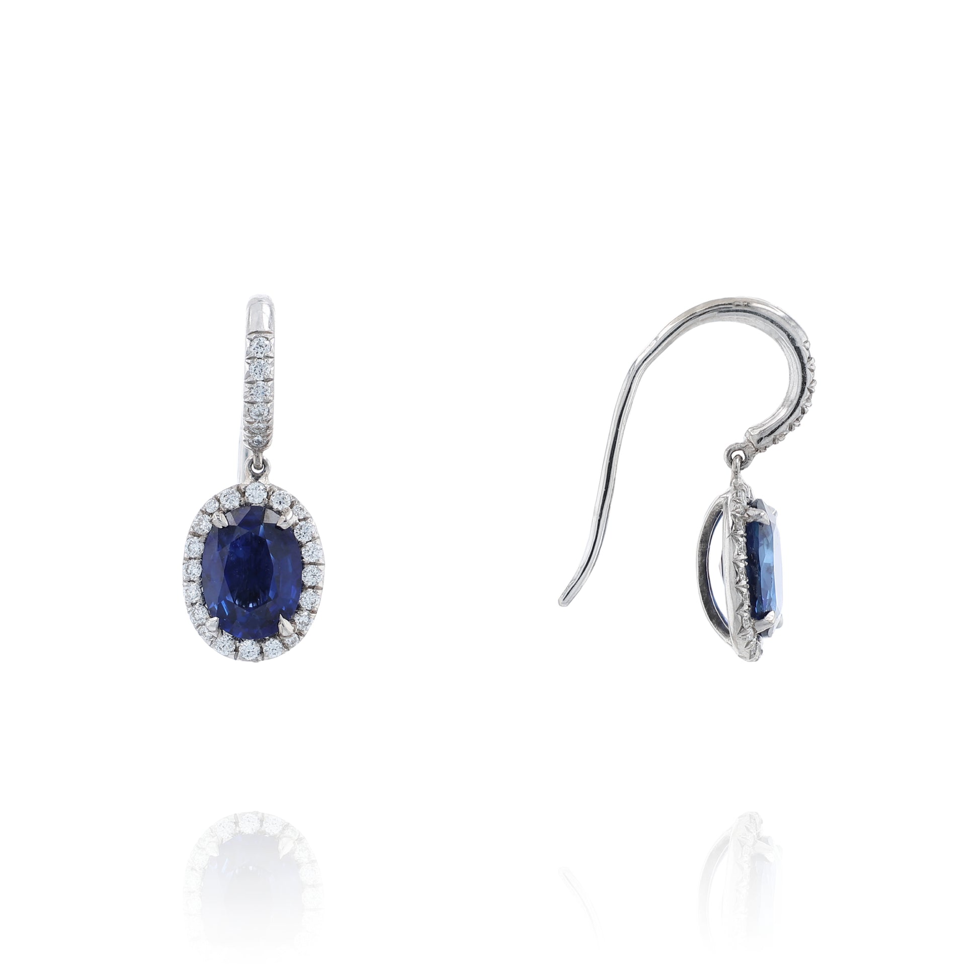 Pair of white gold diamond halo drop earrings with oval blue sapphire centers on a white background