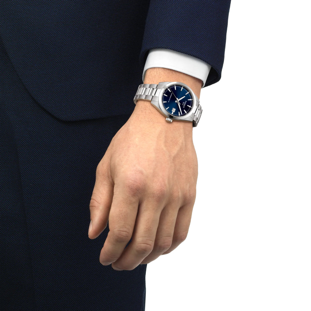 Hand wearing a silver Tissot watch with a blue dial on a white background
