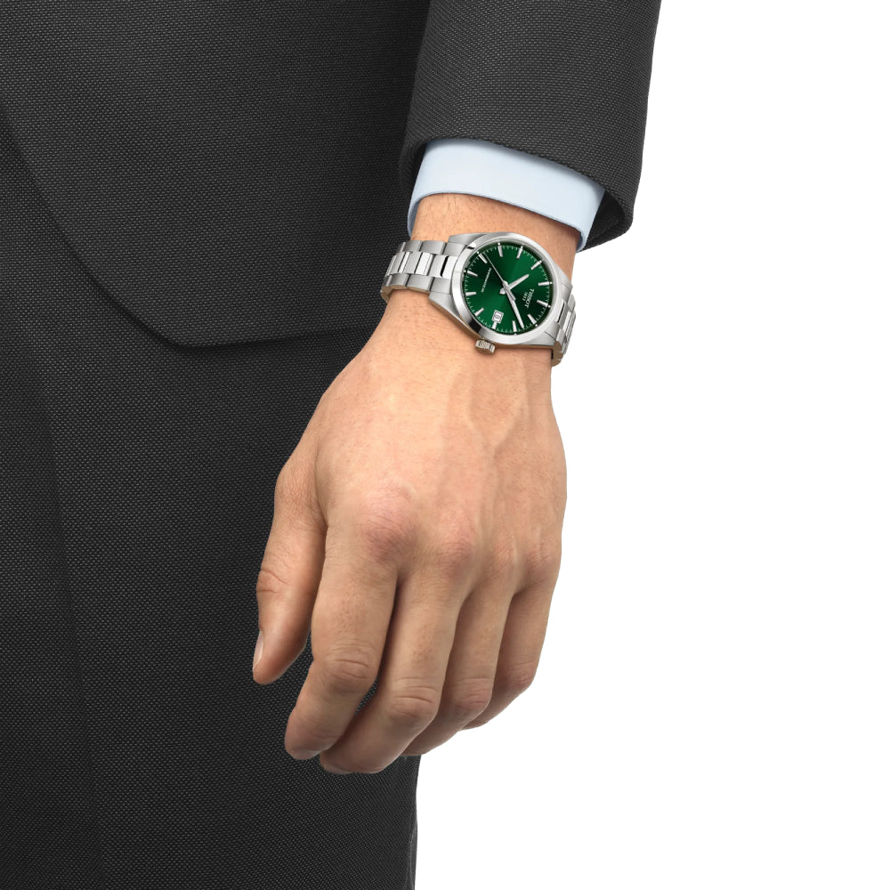 Man in a suit wearing a silver Tissot watch with a green dial on a white background