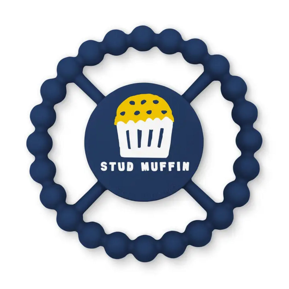 A navy blue silicone baby teether with a wavy outer edge and four spokes, featuring a central circle with a yellow and white stud muffin illustration and the text 'STUD MUFFIN'.
