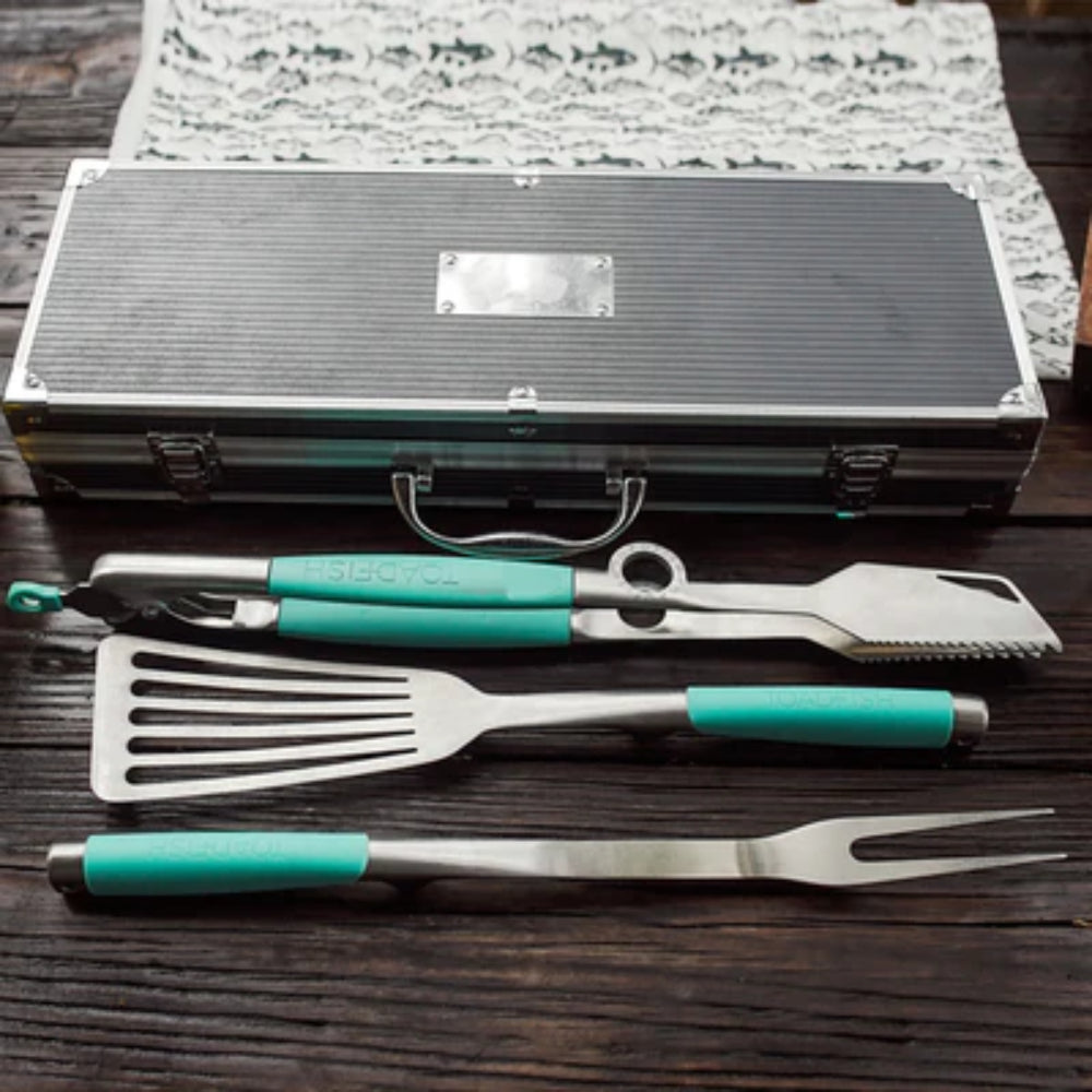 Set of barbecue tools with turquoise handles on a wooden surface, including a case.