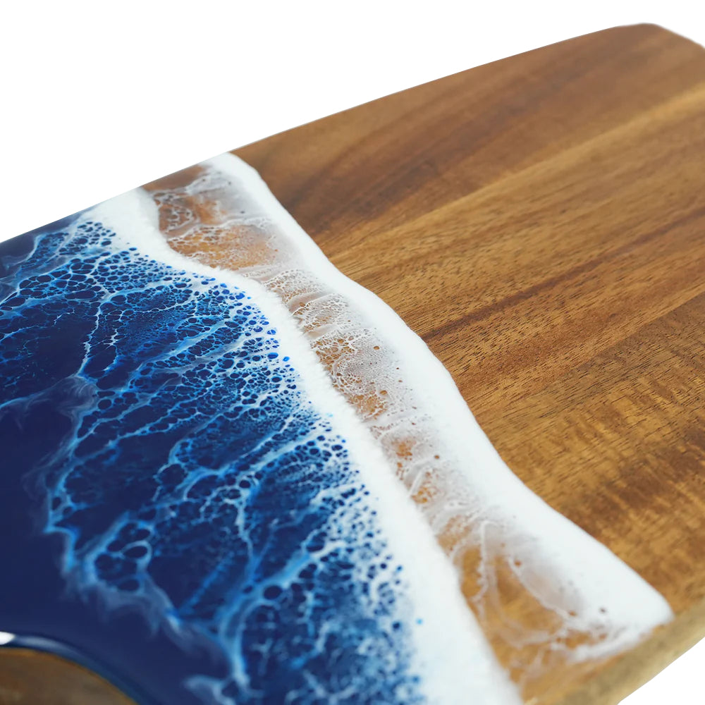 A close up photo of a wooden cutting board with blue resin ocean surf edge and 'Toadfish' branding on a white background.