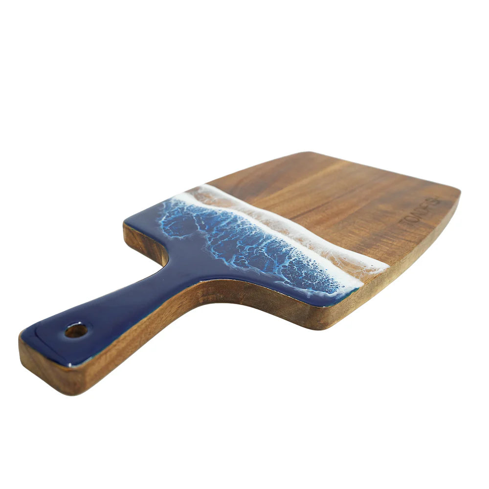 Angled side photo of a wooden cutting board with blue resin ocean surf edge and 'Toadfish' branding on a white background.